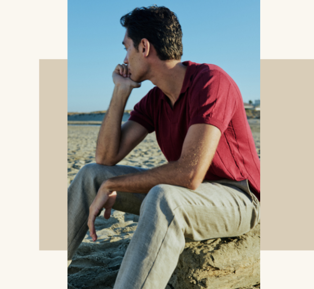 Modello seduto sulla sabbia con t-shirt rossa e pantaloni beige, atmosfera estiva e rilassata